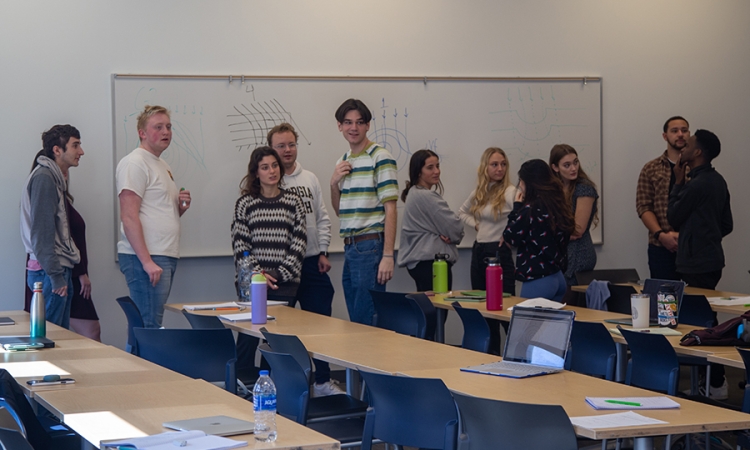 A dozen students in front of a white board in a classroom 