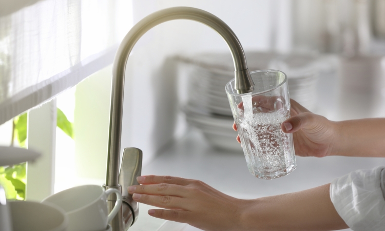 A person filling a drinking glass with water from a faucet 