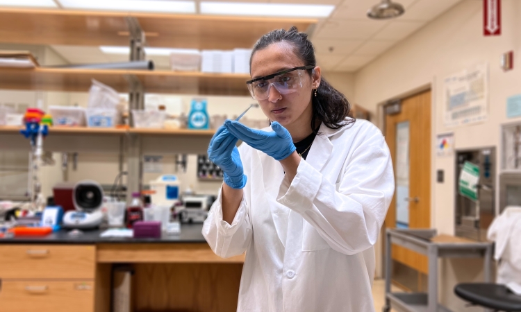 A woman wearing protective equipment holds a pipette in a laboratory