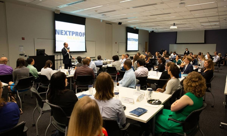 A group of people sitting at tables look at a man with a microphone giving a presentation 