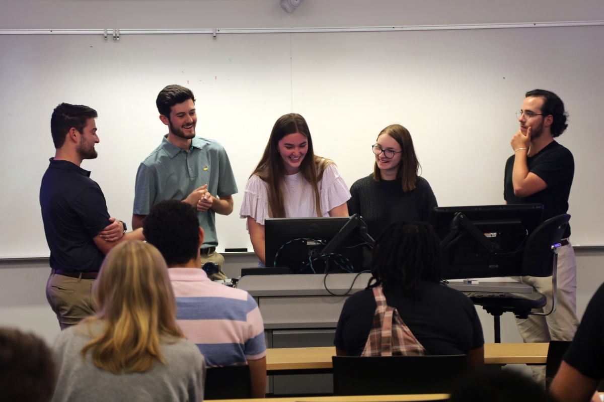 A group of students stands in front of a computer screen