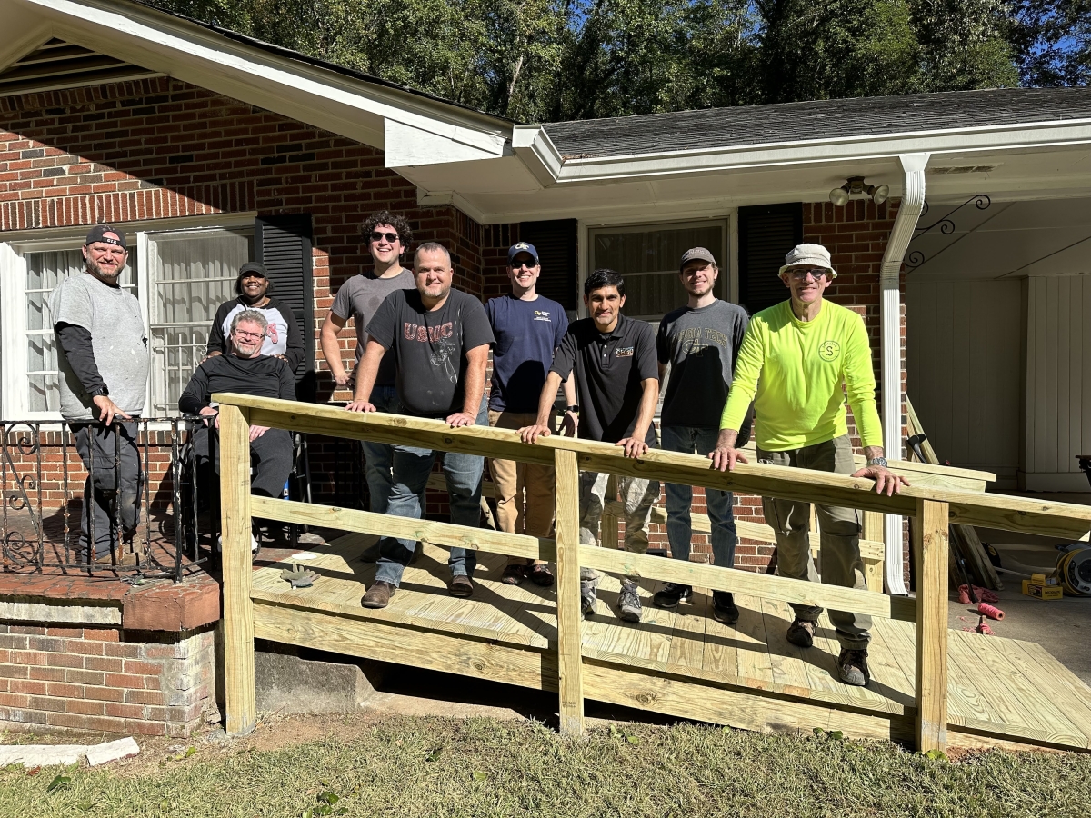 Crew of faculty, staff and students pose on newly constructed ramp in front of house