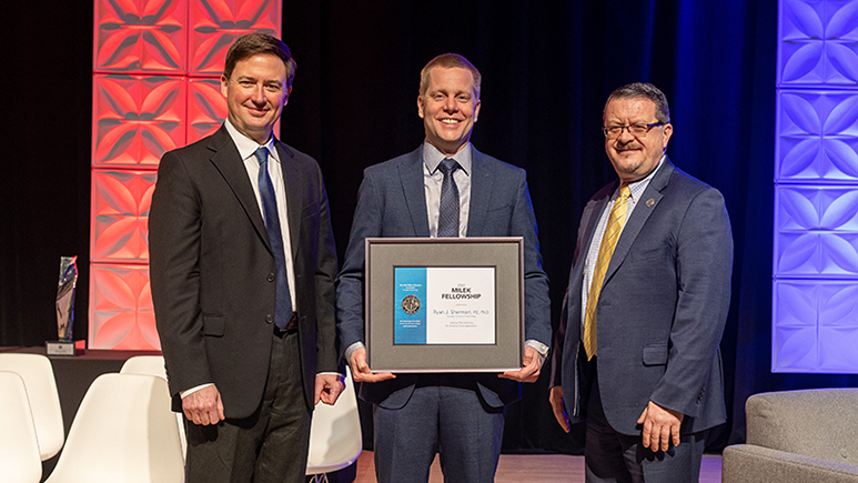 Ryan Sherman posing with a framed award alongside two other men