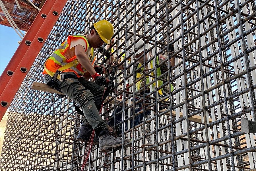 A man in a yellow hard hat and orange reflective vest works on a concrete sensor installation