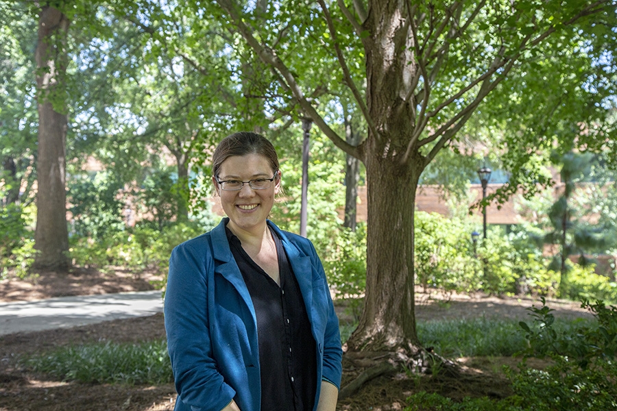 Emily Grubert is wearing a blue blazer and standing outdoors in front of a tree.