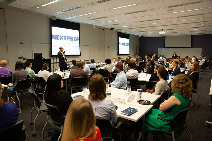 A group of people sitting at tables look at a man with a microphone giving a presentation 