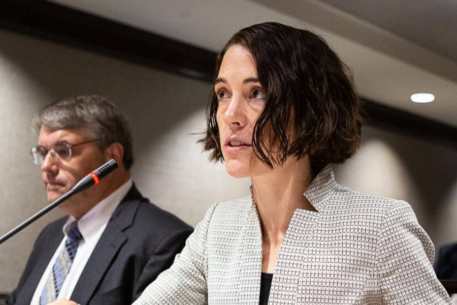 Gretchen Goldman wears a light blazer and sits before a microphone