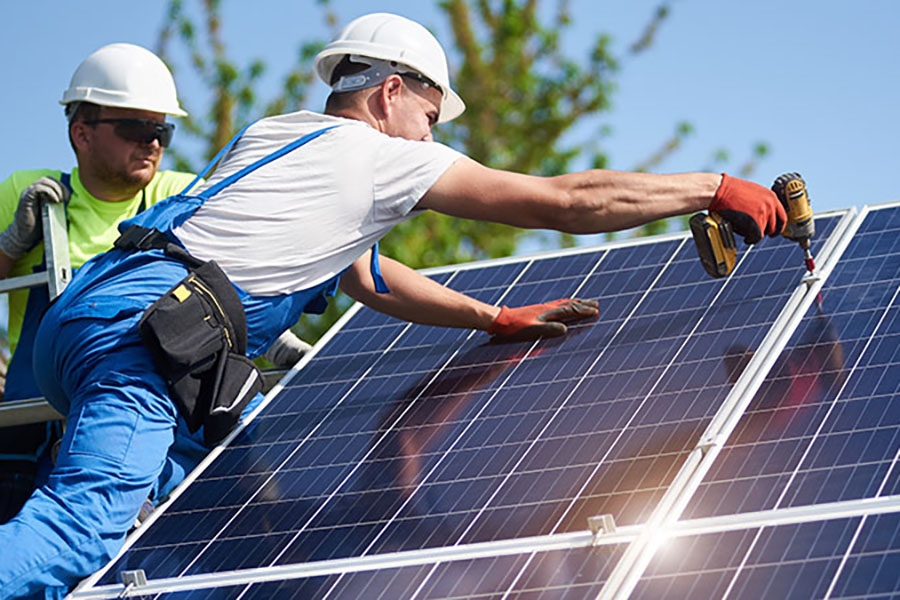 two men wearing white hard hats install solar panels 